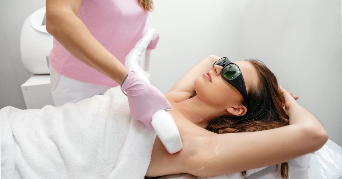 Woman in protective eyewear getting underarm laser hair removal in Sykesville, MD from a technician in pink gloves.